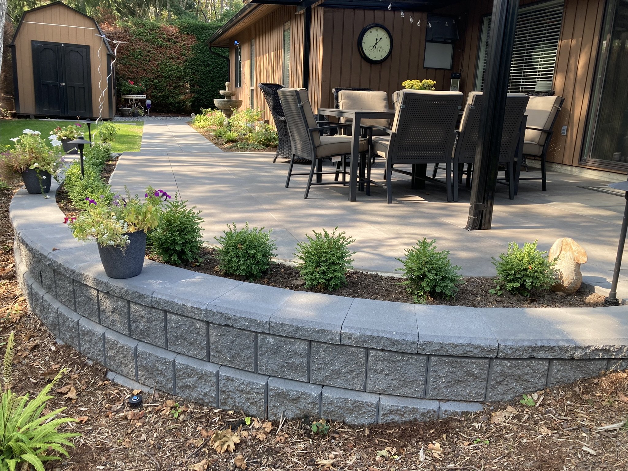 A curved block retaining wall with new boxwood planting beside a porcelain patio